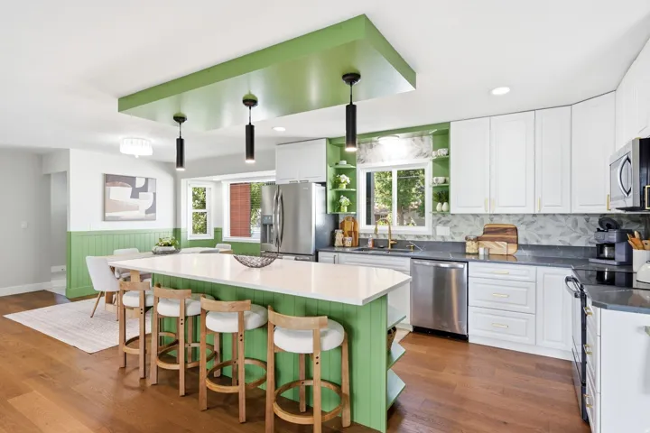 Spacious kitchen with a central island featuring a white countertop, stainless steel appliances, white cabinetry, and hardwood flooring