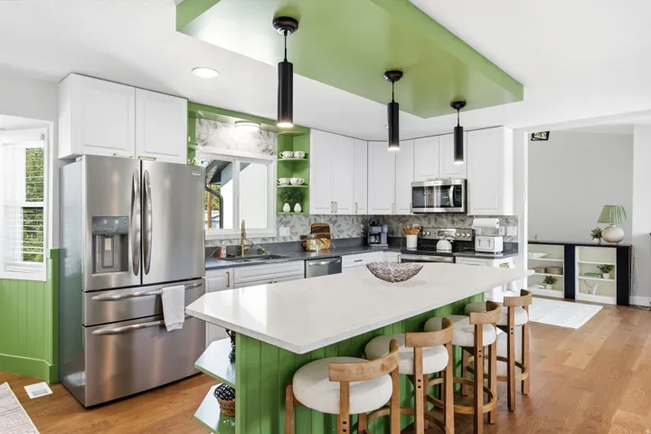 Kitchen featuring stainless steel appliances, white cabinetry, a central island with a light-colored countertop, three pendant lights, and wood-finish flooring