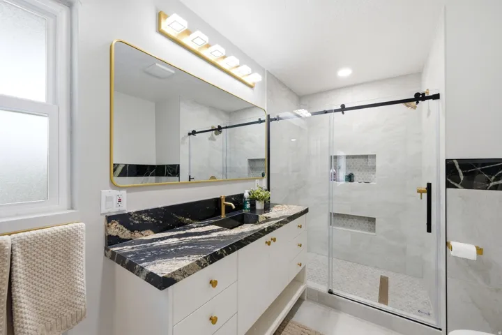 Bathroom featuring a single vanity with a black and gold patterned countertop, a gold-framed mirror, and a gold-finished lighting fixture