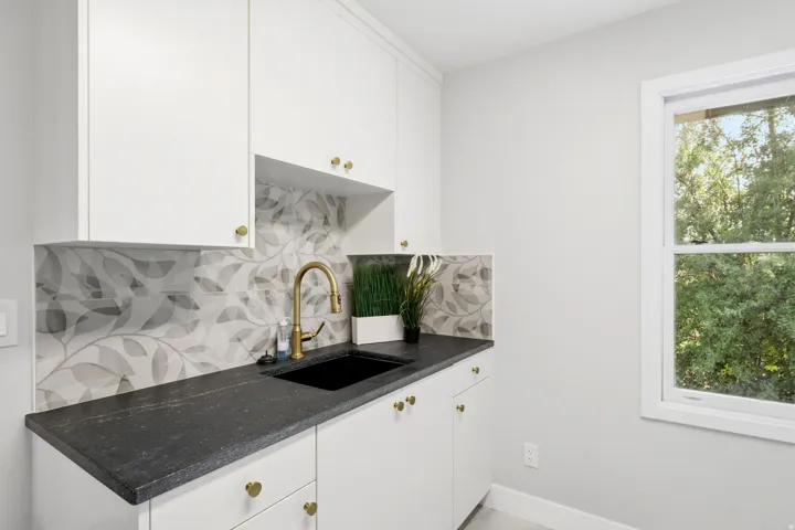 White cabinetry with gold-toned hardware, dark-toned countertop, black undermount sink, and a gold-toned gooseneck faucet