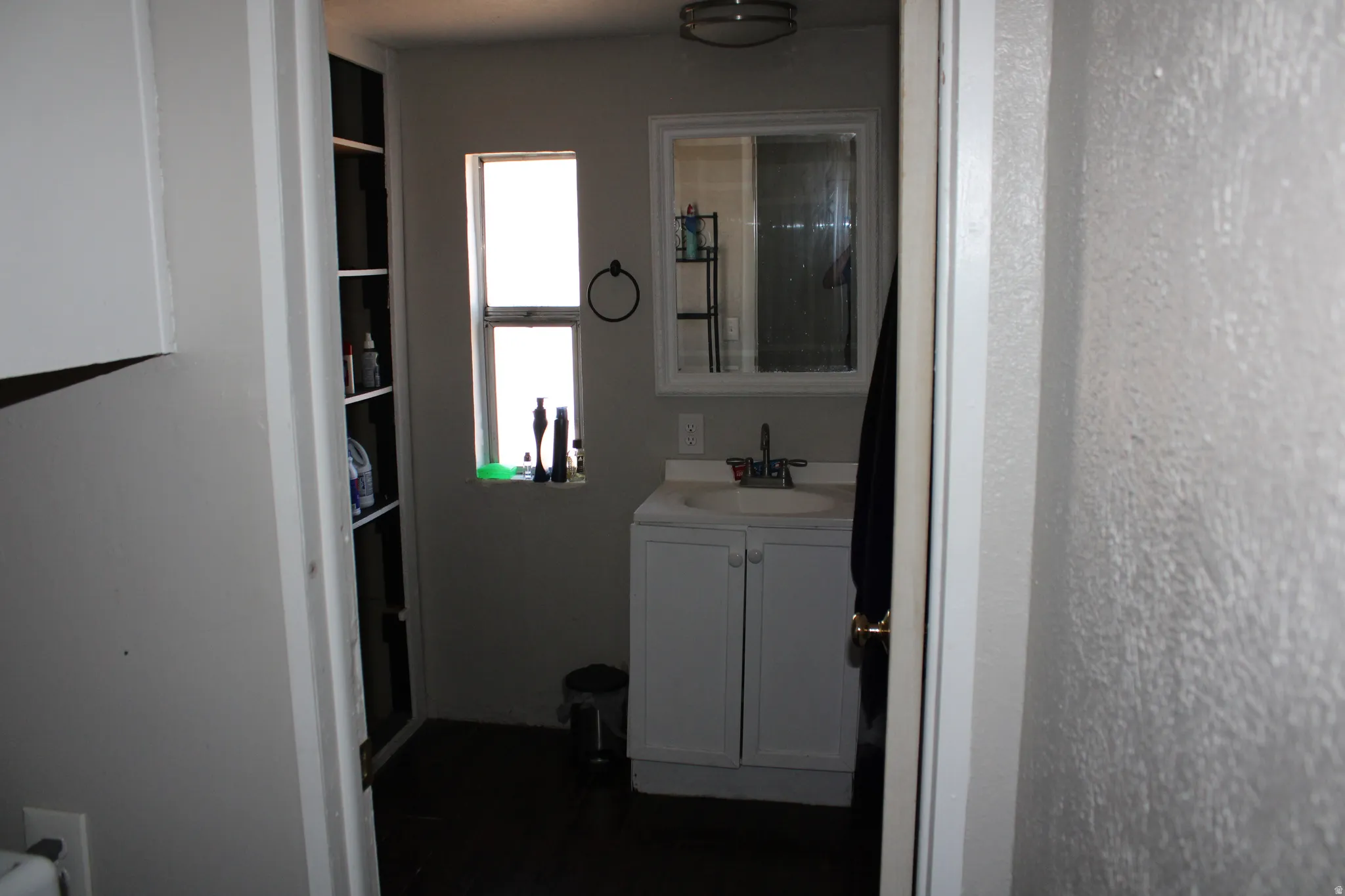 Built-in shelving, window for natural light, white vanity with storage, wall-mounted mirror, and overhead light fixture
