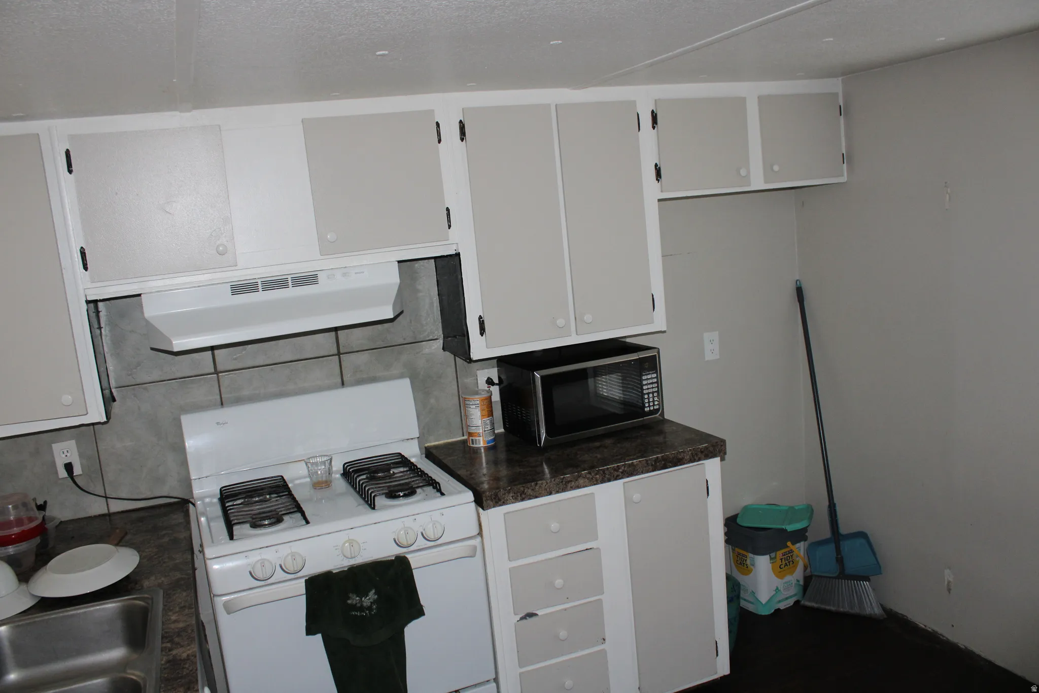 Compact kitchen with upper and lower cabinetry, laminate countertops, a built-in range hood, and a gas range