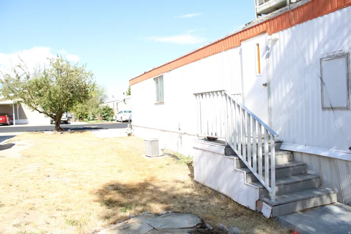 Exterior featuring white corrugated siding, orange trim, outdoor stairs with metal railings, and a visible air conditioning unit