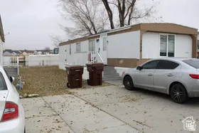 White siding exterior with a brown trim roof, visible steps to entry, and a concrete driveway