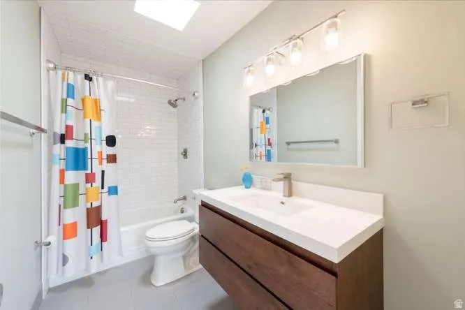 Skylight with a full bath, subway tile shower surround, contemporary wood-finish vanity, and integrated sink