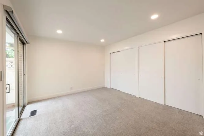 Recessed lighting illuminates the room, featuring a sliding glass door and soft carpet flooring