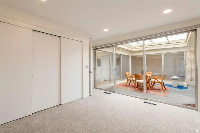 Recessed lighting, light-toned carpeting, white sliding closet doors, and a glass-enclosed outdoor courtyard with a skylight