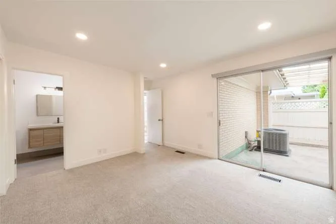 Recessed lighting, light-toned carpeting, sliding glass patio door, modern floating vanity with a vessel sink, and an outdoor patio area