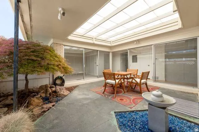 Enclosed patio featuring a translucent roof, concrete flooring, and a water feature with blue glass stones