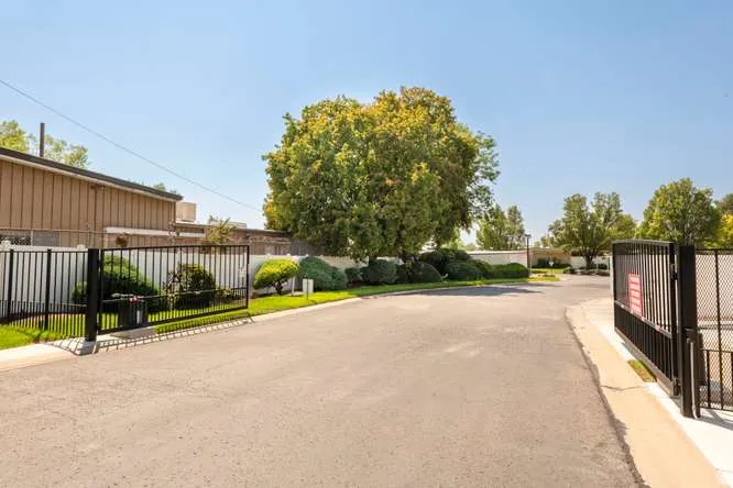 Gated entrance featuring black metal fencing, asphalt paving, and mature trees
