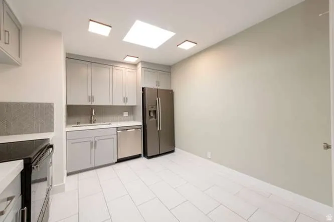 Kitchen featuring gray cabinetry, stainless steel appliances, white countertops, and a full-height geometric tile backsplash