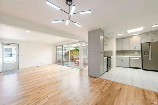 Light wood-finish flooring, recessed lighting, and a modern chandelier illuminate this open-concept area