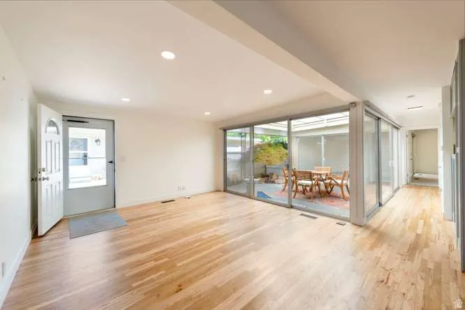 Recessed lighting, wood-finish flooring, white walls, full-height glass panels, and a courtyard with a hardscaped patio