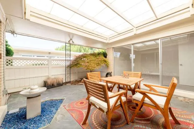 Covered patio with a translucent roof system, featuring a privacy lattice fence, brick wall, and concrete flooring