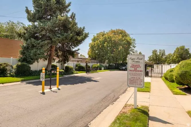 Gated entry with a speed limit sign, mature trees, and a manicured hedge