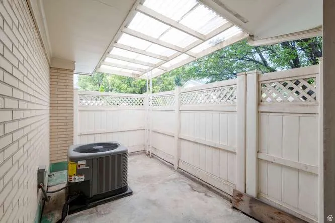 Brick exterior wall, covered patio with translucent roofing, concrete flooring, and white lattice fencing