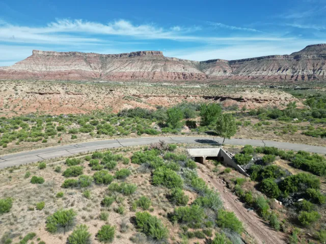 Mountain backdrop with layered rock formations, expansive terrain with varied foliage, and a paved roadway