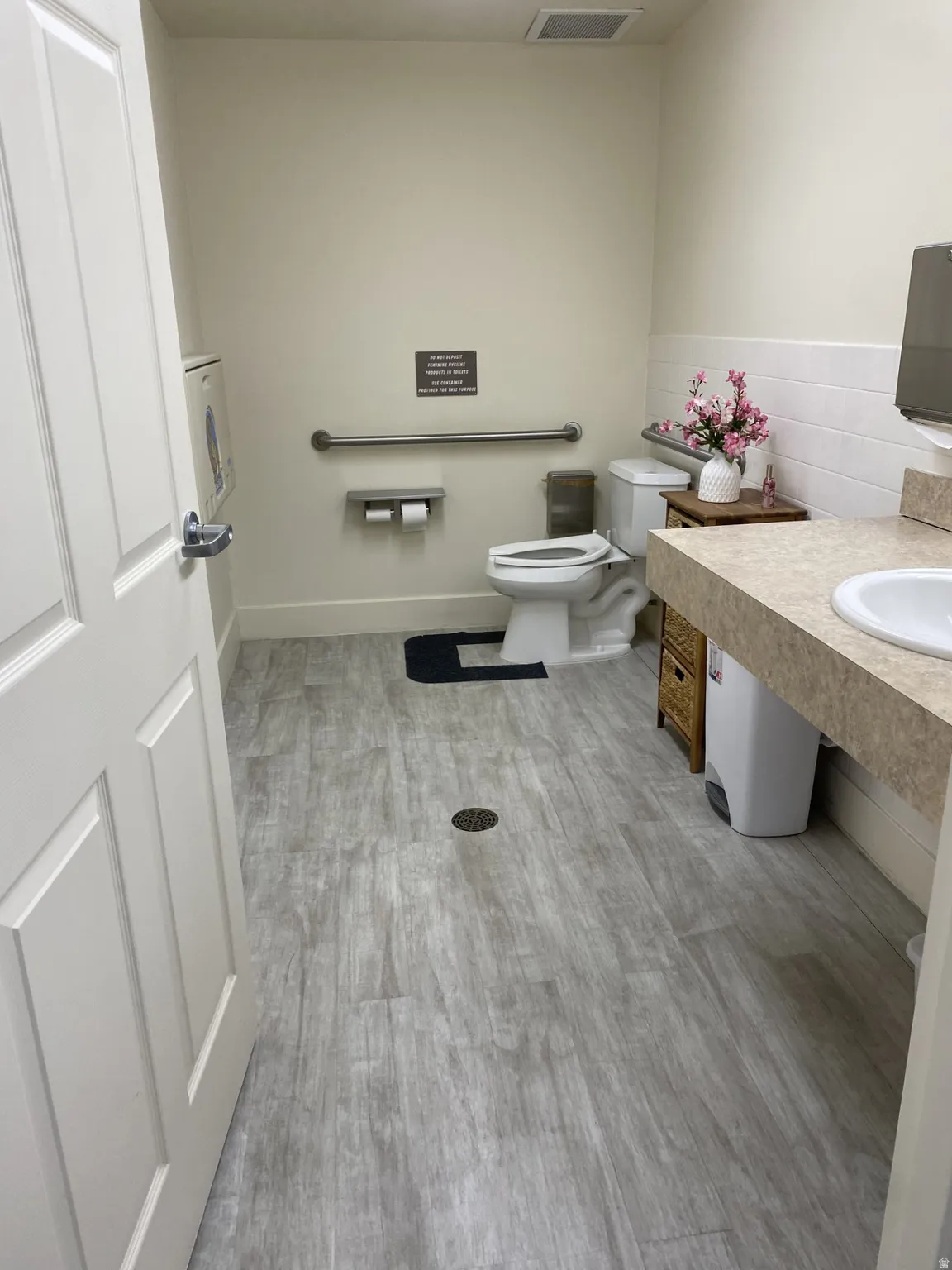 Restroom featuring wood-finish flooring, a white vanity with a single basin sink, a wall-mounted grab bar, and a toilet