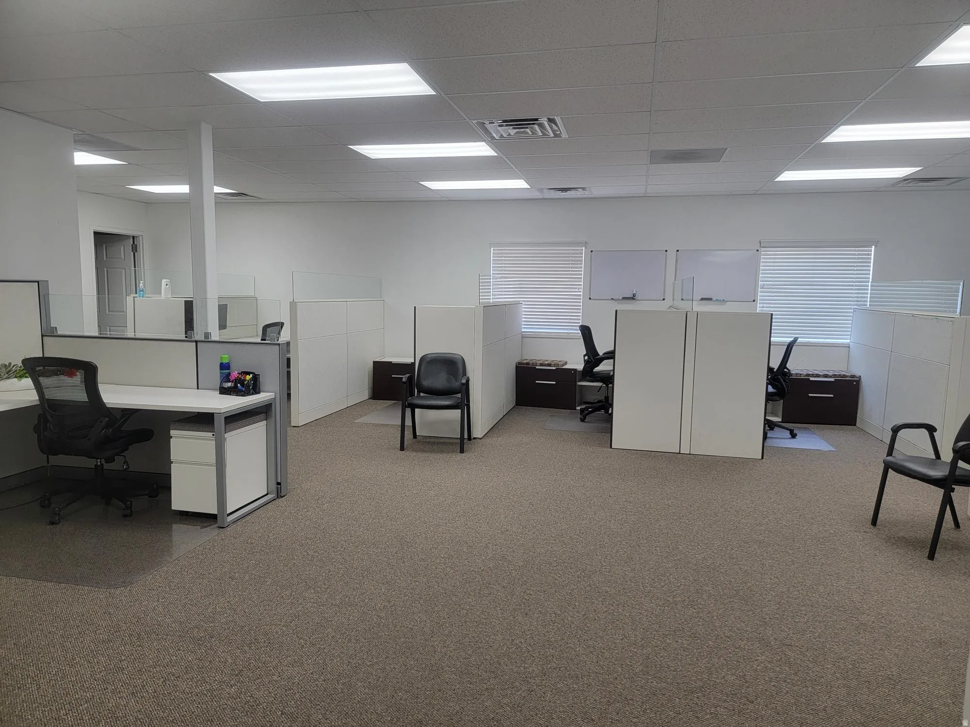 Open-plan office space featuring carpeted flooring and multiple workstations with privacy panels. Most Furniture included