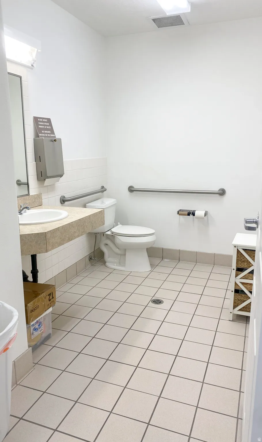 Restroom featuring a single vanity, white toilet, grab bars, and light-toned square tile flooring