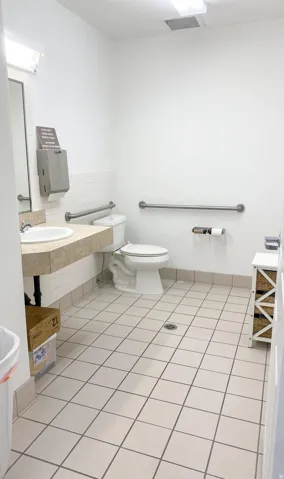 Restroom featuring a single vanity, white toilet, grab bars, and light-toned square tile flooring