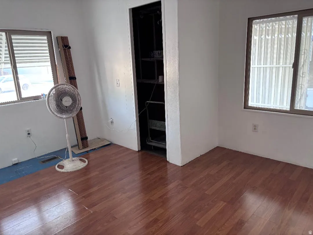 Wood-finish flooring, two windows with blinds, built-in open shelving, and white painted walls