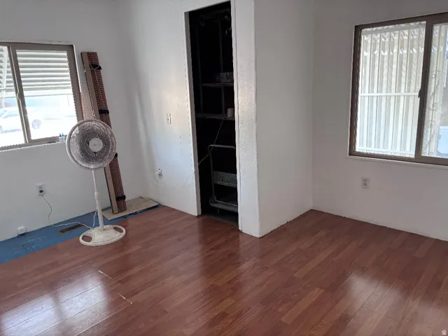 Wood-finish flooring, two windows with blinds, built-in open shelving, and white painted walls