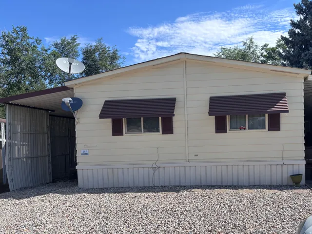 Exterior featuring light-colored siding, two windows with brown shutters, and matching brown awnings