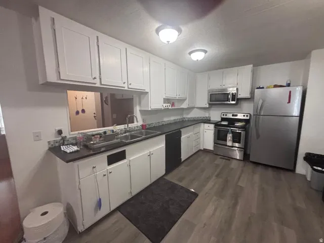 Galley kitchen featuring white cabinetry, dark countertops, stainless steel appliances, and wood-finish flooring