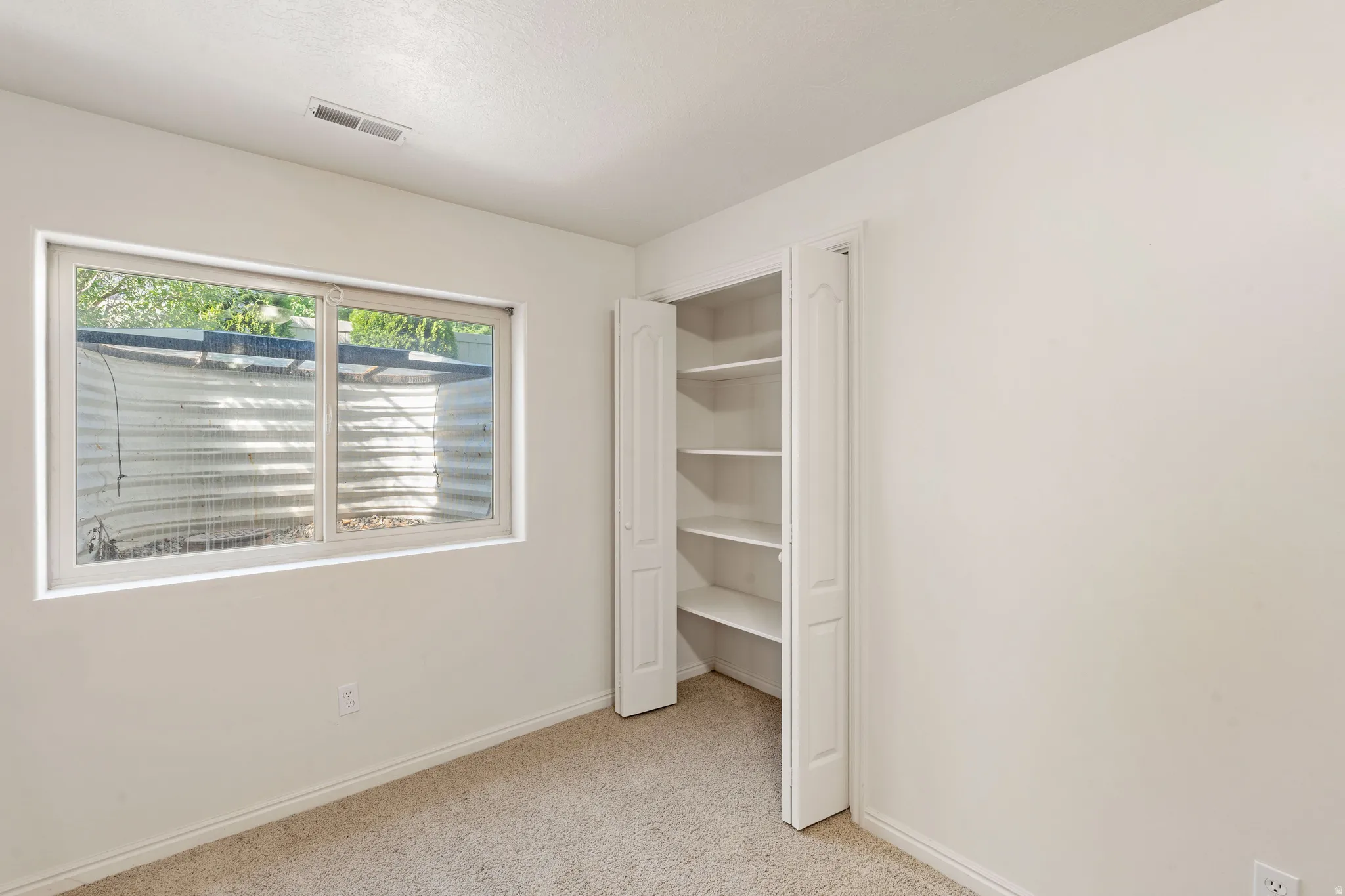 Carpeted flooring, white walls, built-in shelving, and a dual-pane window