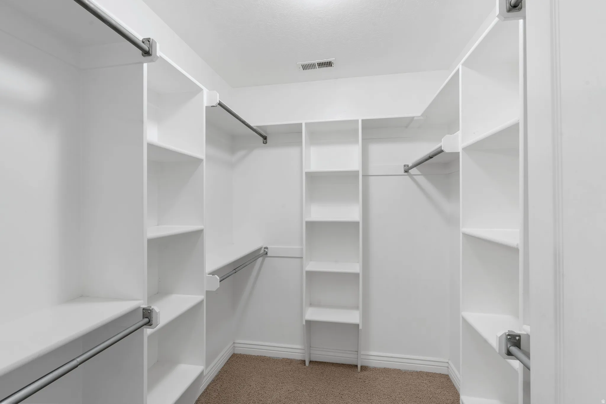 Walk-in closet with integrated white shelving, multiple hanging rods, and light brown carpeting