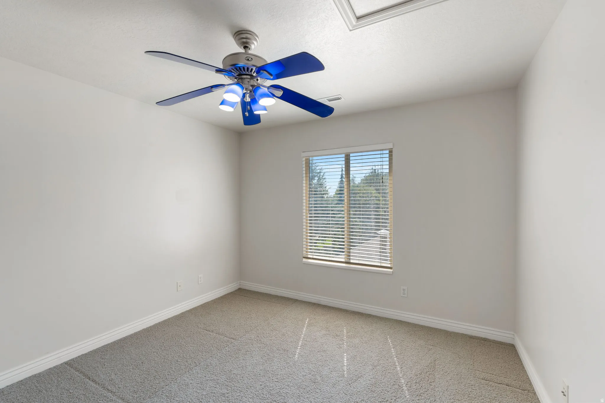 Neutral wall finishes, recessed window with blinds, ceiling-mounted fan with light fixture, and textured carpeting