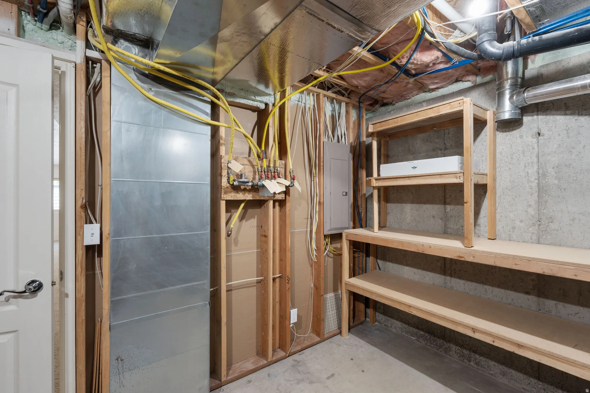Utility area featuring exposed concrete walls, exposed ceiling joists, and built-in wood shelving