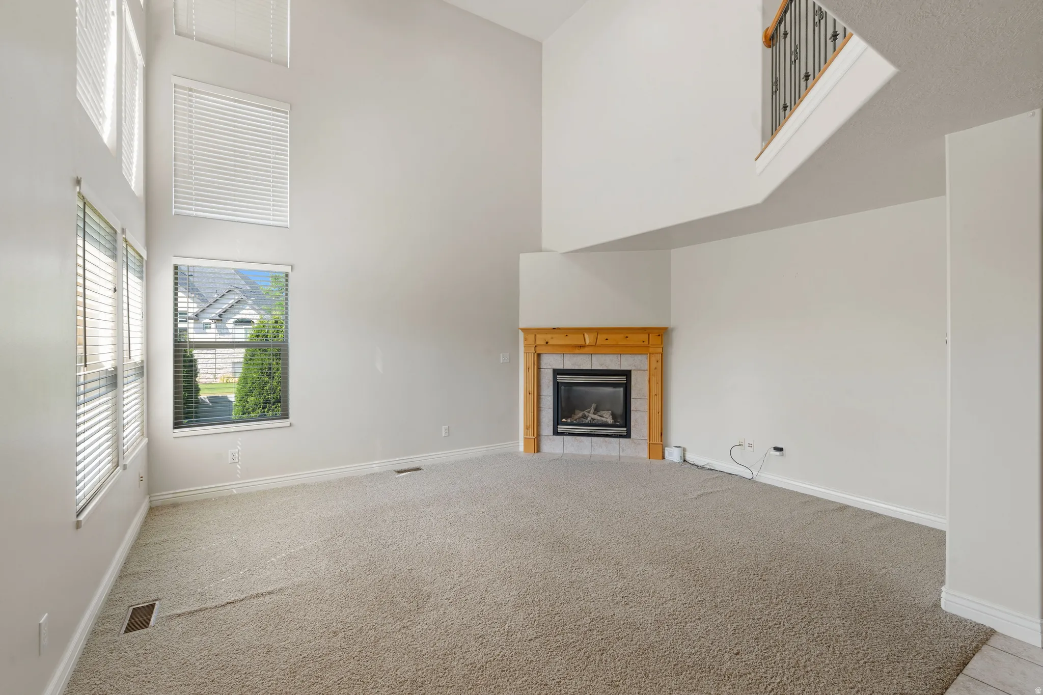 Vaulted ceiling living area featuring multiple windows, a corner fireplace with wood mantel, and an interior balcony with metal balusters