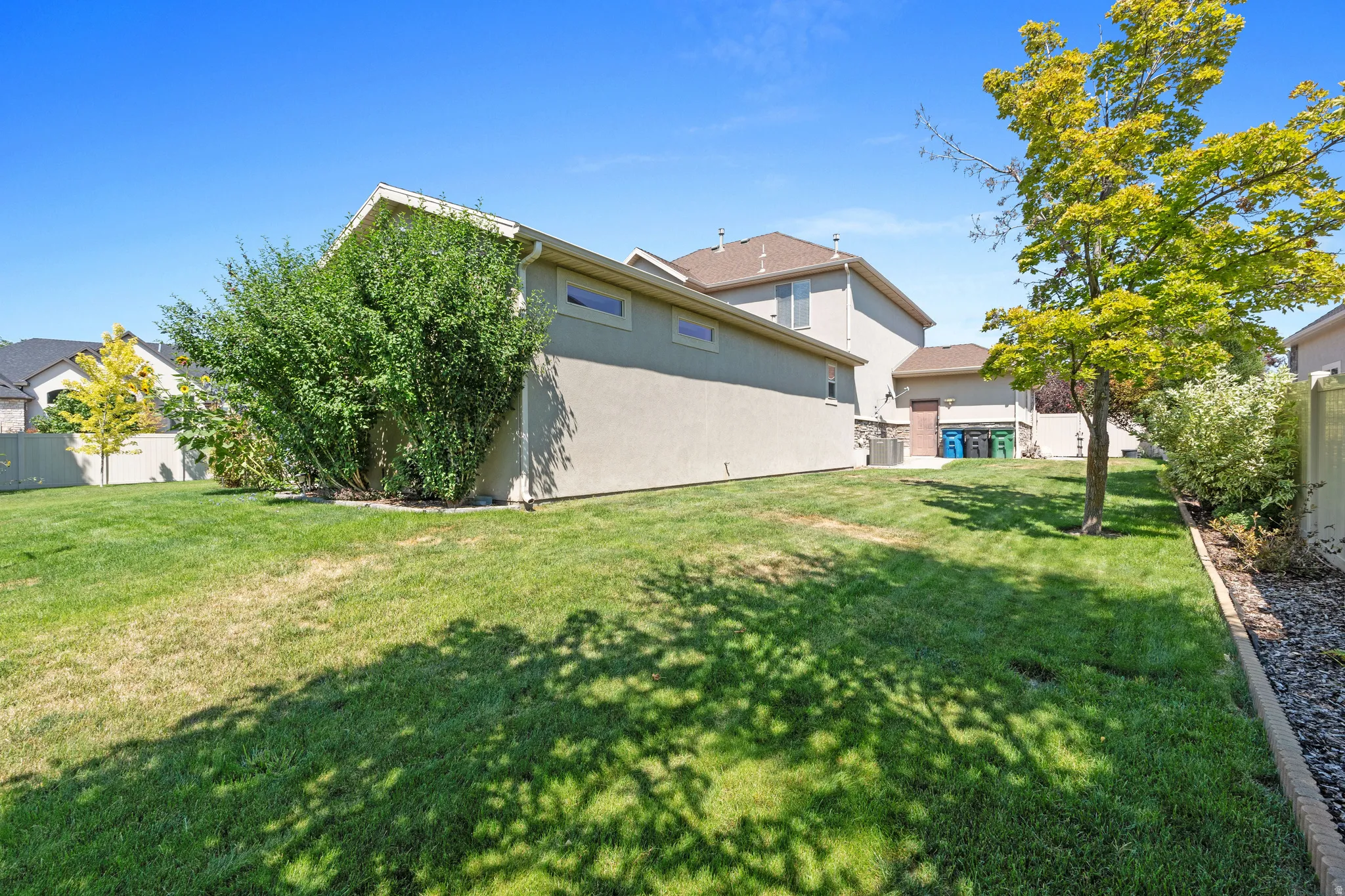 Expansive grass lawn with mature shrubbery and established trees, bordered by a concrete retaining edge