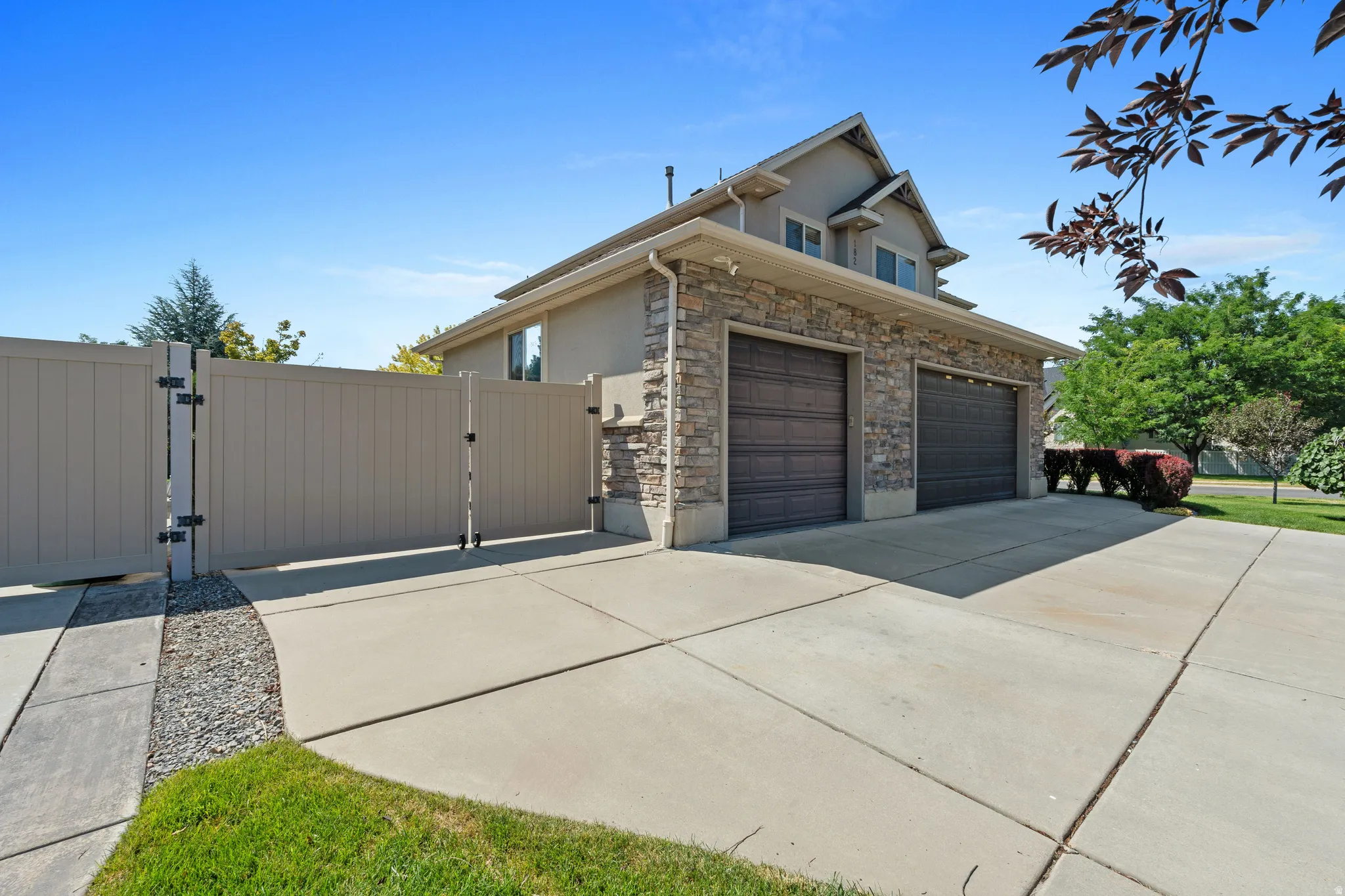 Attached two-car garage with wood-finish doors, stone facade accents, and an expansive concrete driveway
