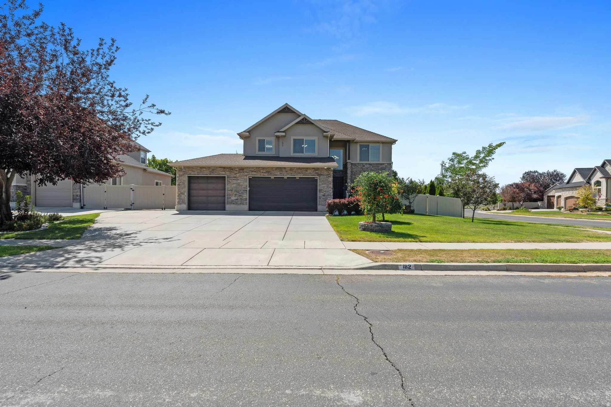 Two-story home with stone and siding exterior, multi-car driveway, and integrated garage doors