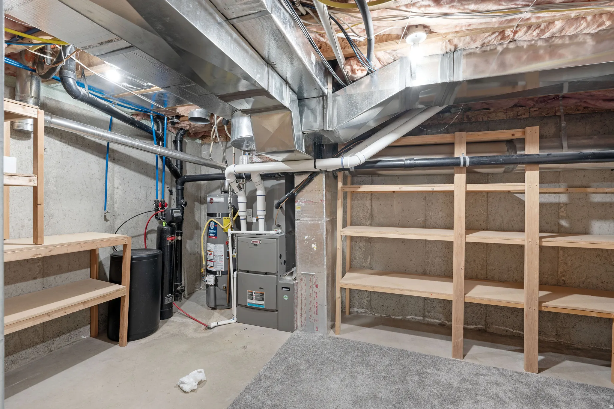 Utility space with exposed ductwork, concrete flooring, built-in wooden shelving, and a visible water heater and furnace