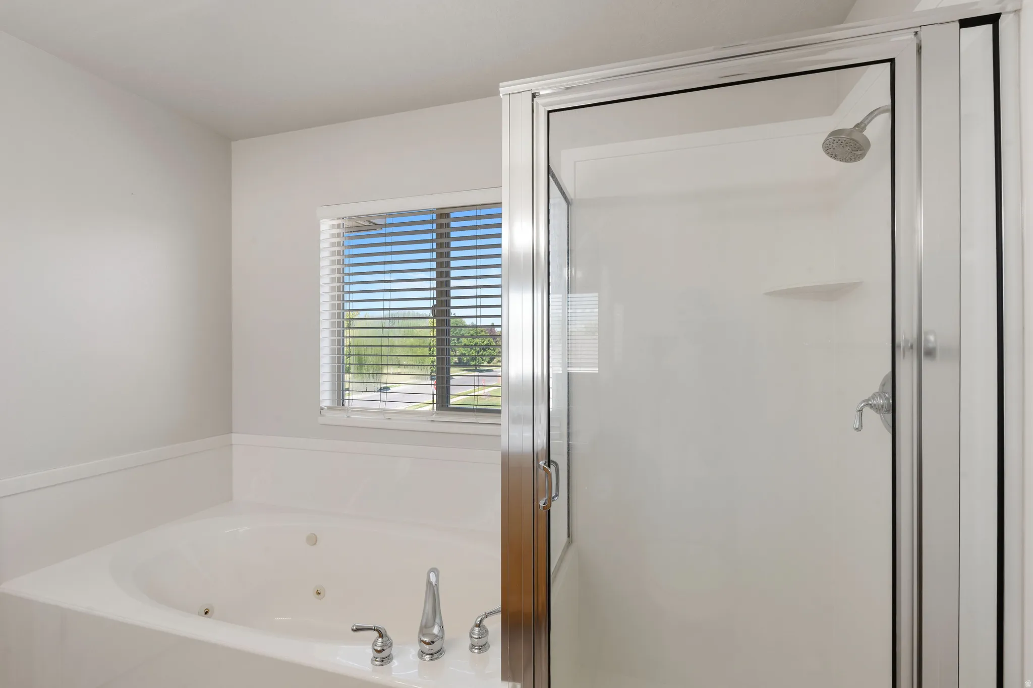 Luxurious spa-inspired ensuite featuring a deep soaking tub with integrated jets, frameless glass shower enclosure with rainfall showerhead, dual vanity setup, and natural light from casement windows with plantation shutters