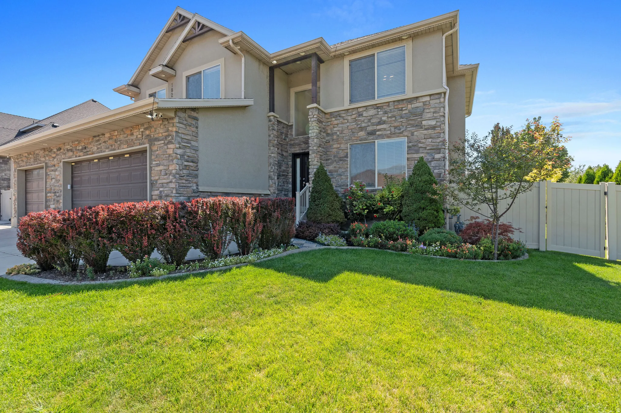 Stucco and stone exterior with a two-car garage, manicured lawn, and mature landscaping