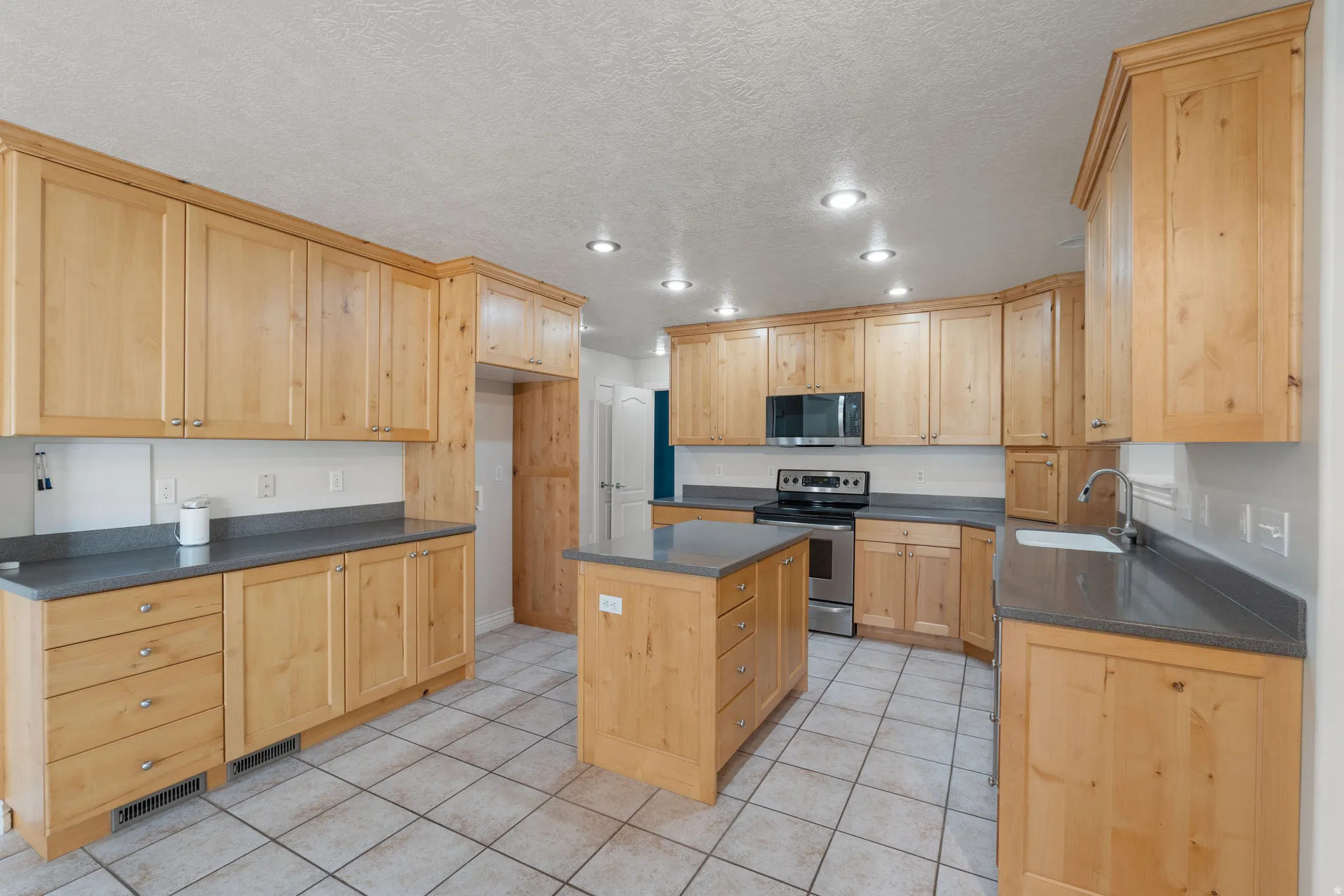 Spacious kitchen featuring extensive light wood cabinetry, gray countertops, a central island with storage, stainless steel appliances, and recessed lighting