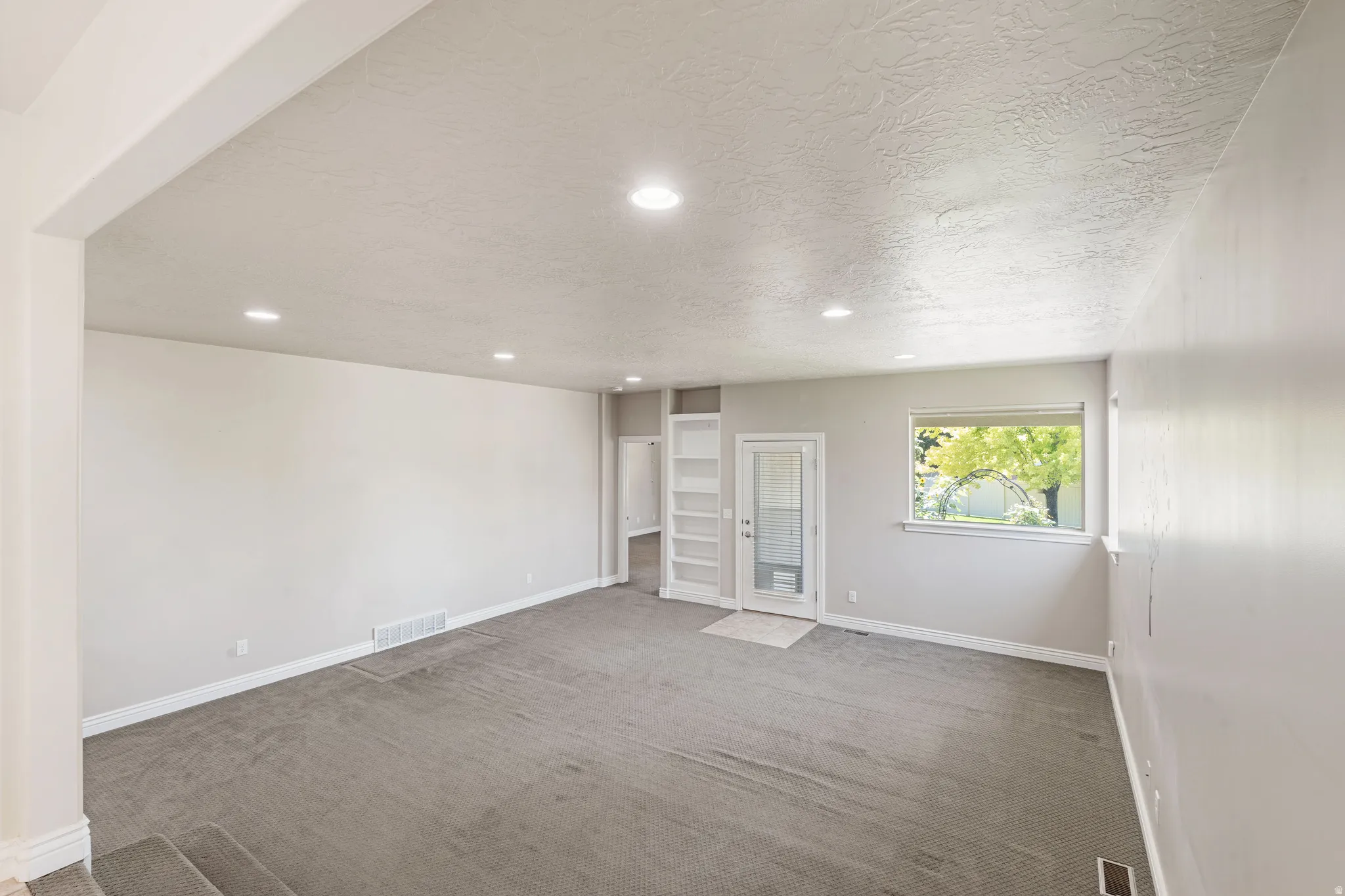 Recessed lighting illuminates the open-concept living space with neutral tone walls and gray carpeting