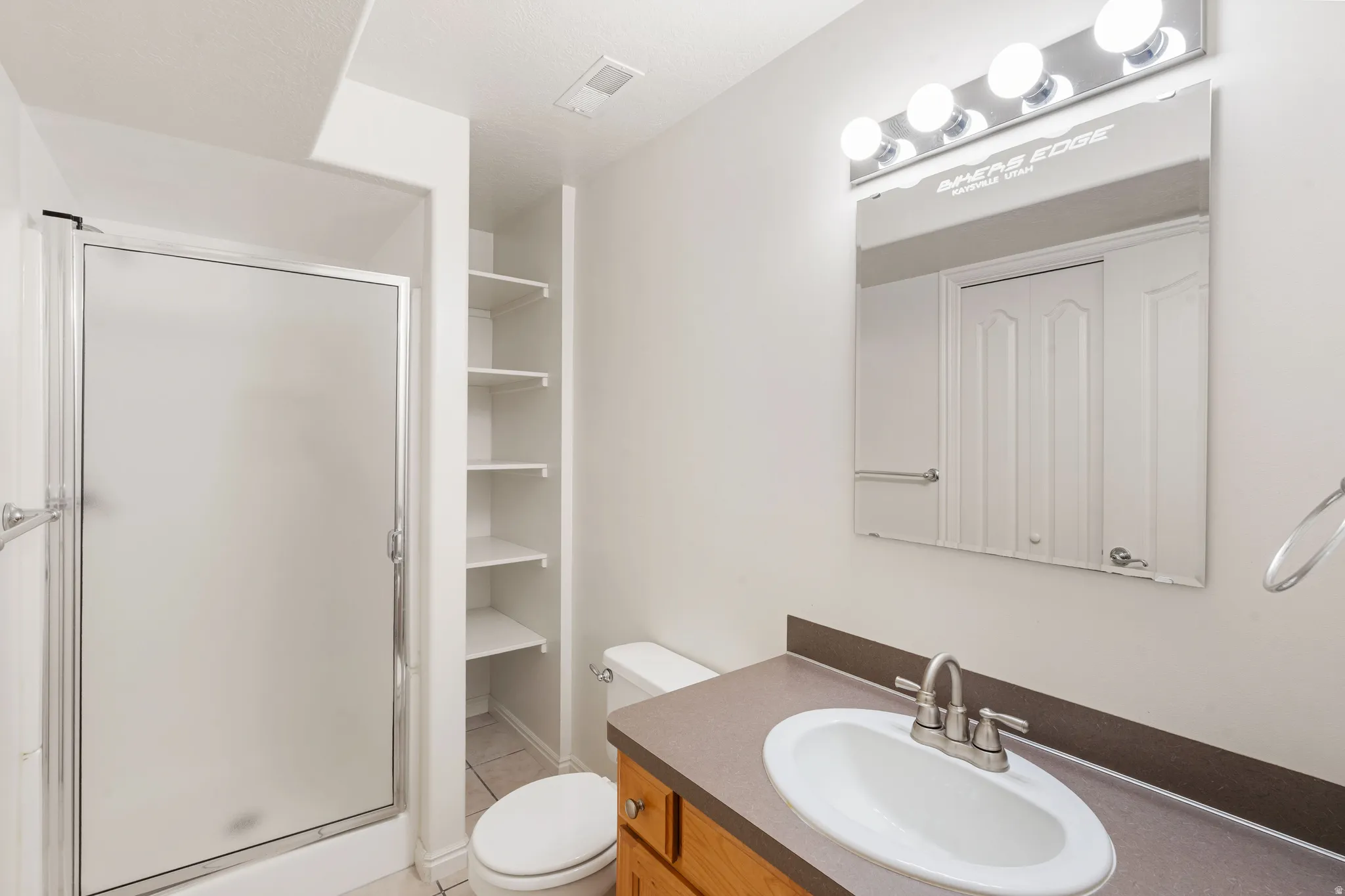 Bathroom featuring a shower with a frosted glass enclosure, built-in shelving, a vanity with an integrated sink, and a mirror