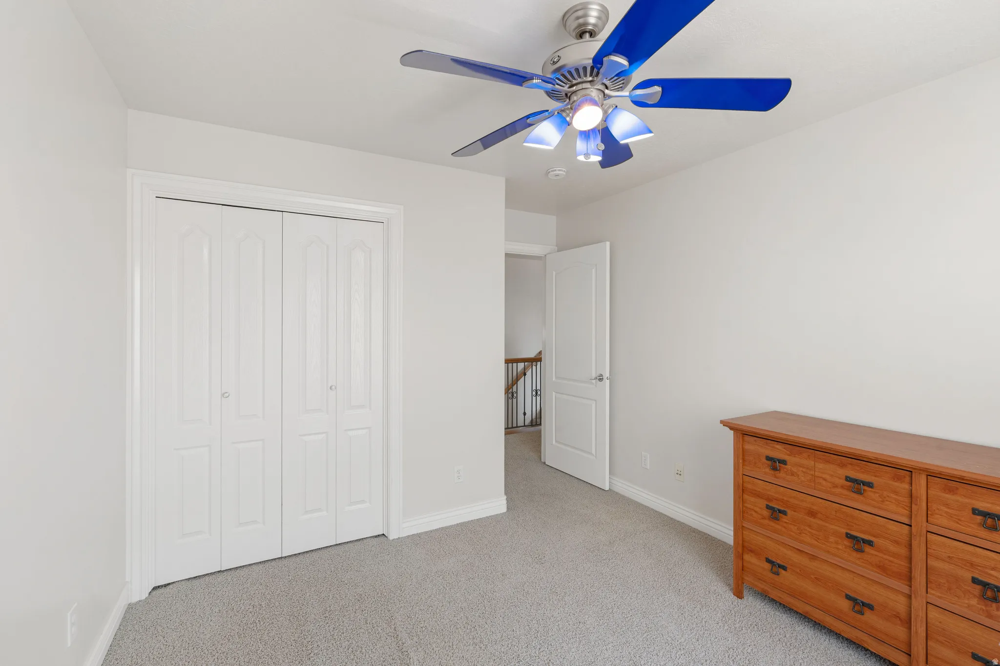 Light gray wall paint, carpeting, bi-fold closet doors, and a ceiling fan with light fixture
