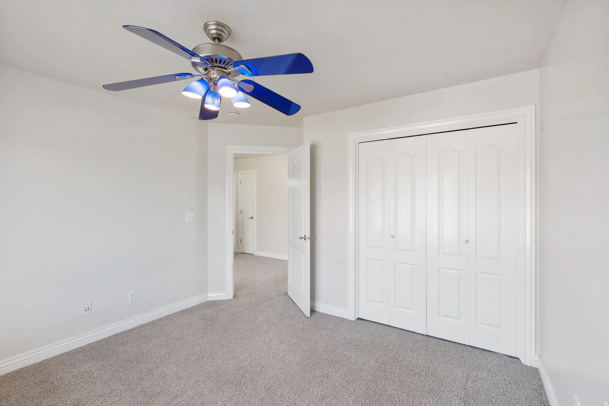 Neutral wall color, light gray carpeting, bi-fold closet doors, and overhead lighting with fan
