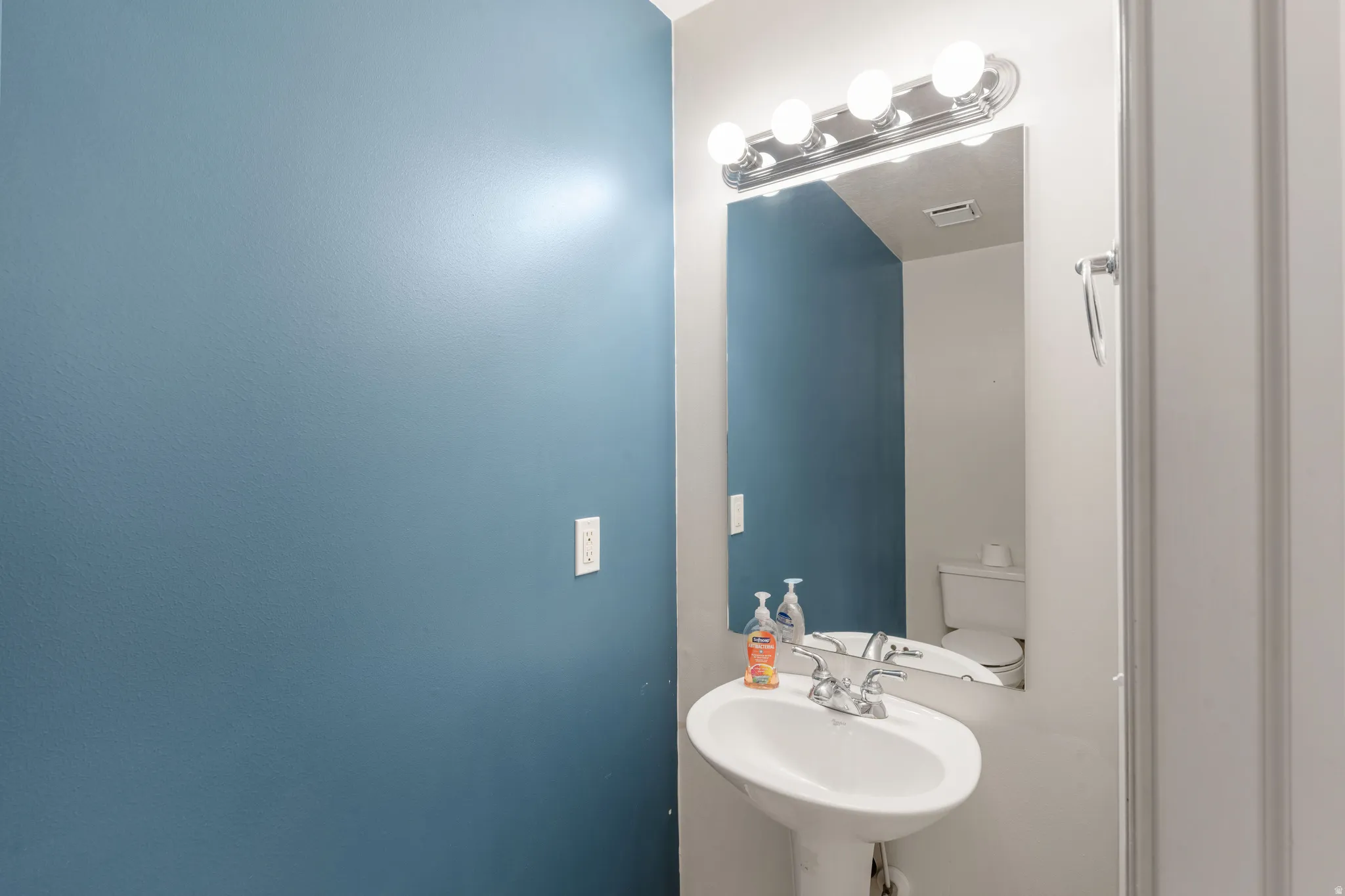 Pedestal sink with chrome faucet, wall-mounted mirror, and vanity lighting fixture