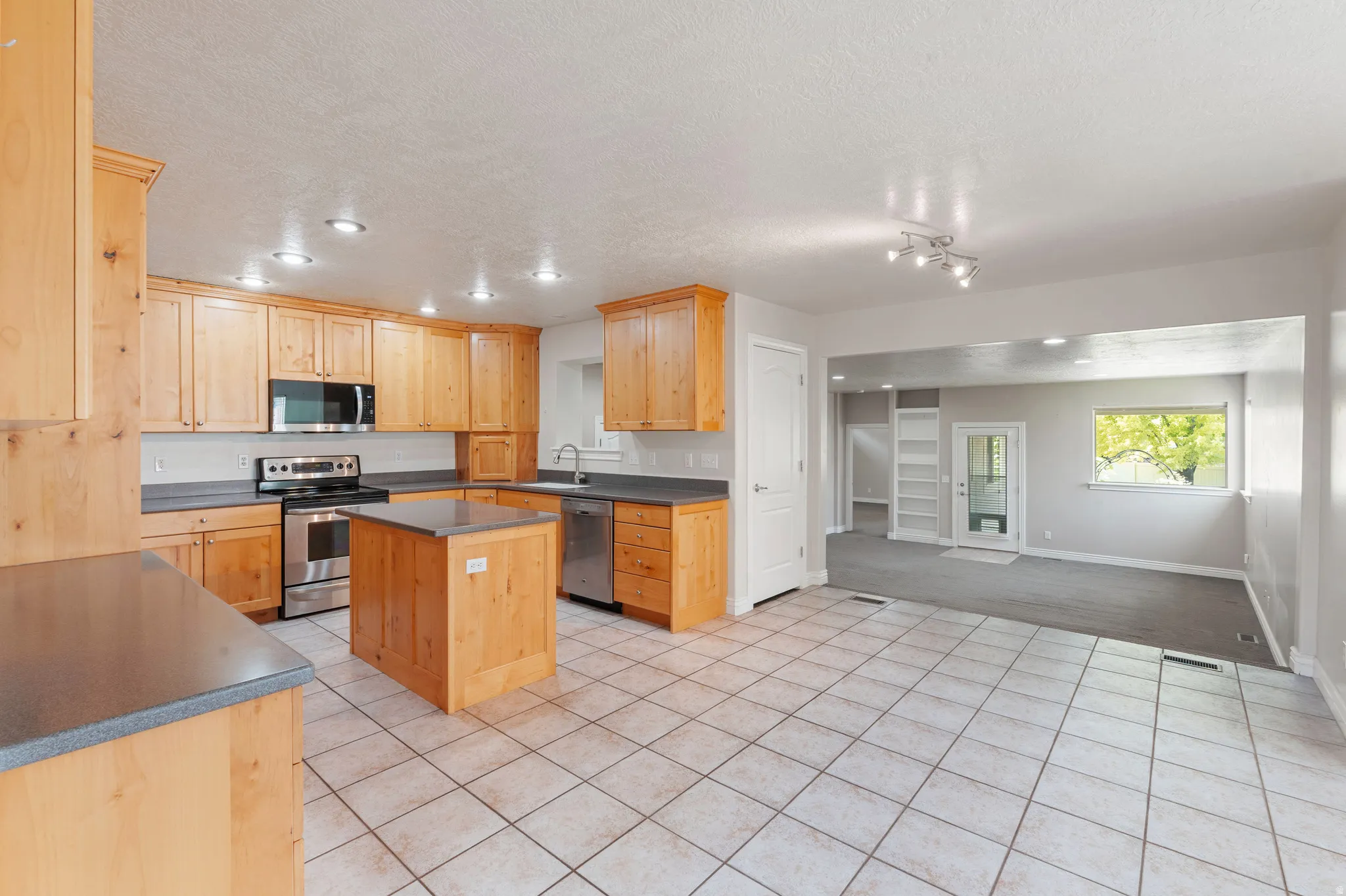 Kitchen featuring wood cabinetry, stainless steel appliances, a center island, and tile flooring
