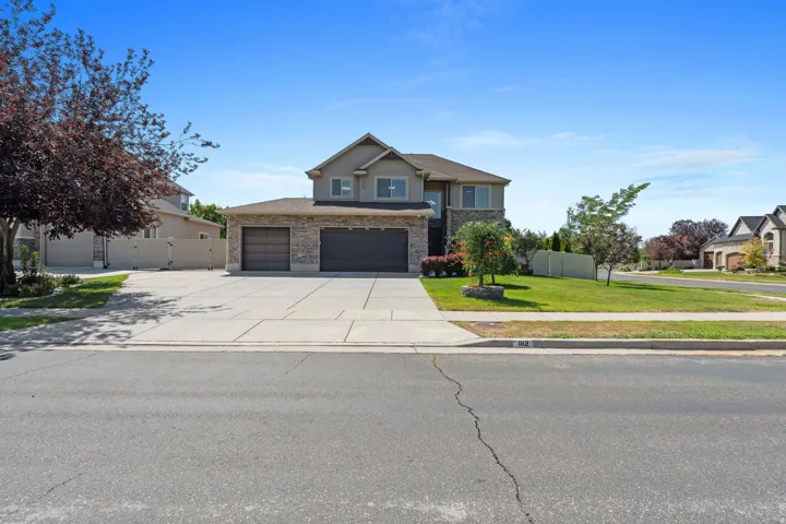 Two-story home with stone and siding exterior, multi-car driveway, and integrated garage doors