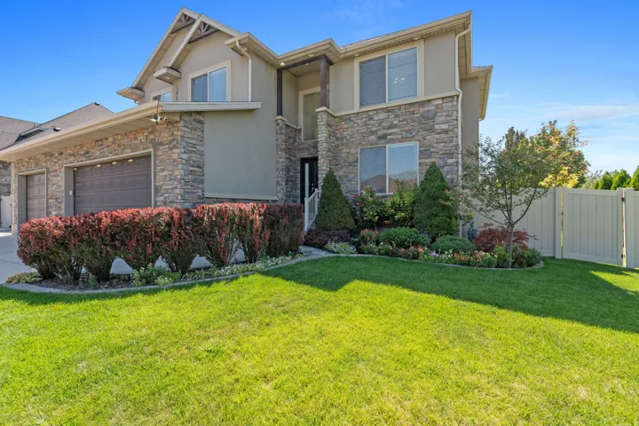 Stucco and stone exterior with a two-car garage, manicured lawn, and mature landscaping