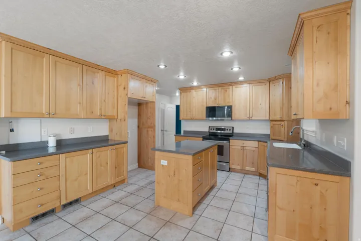 Spacious kitchen featuring extensive light wood cabinetry, gray countertops, a central island with storage, stainless steel appliances, and recessed lighting